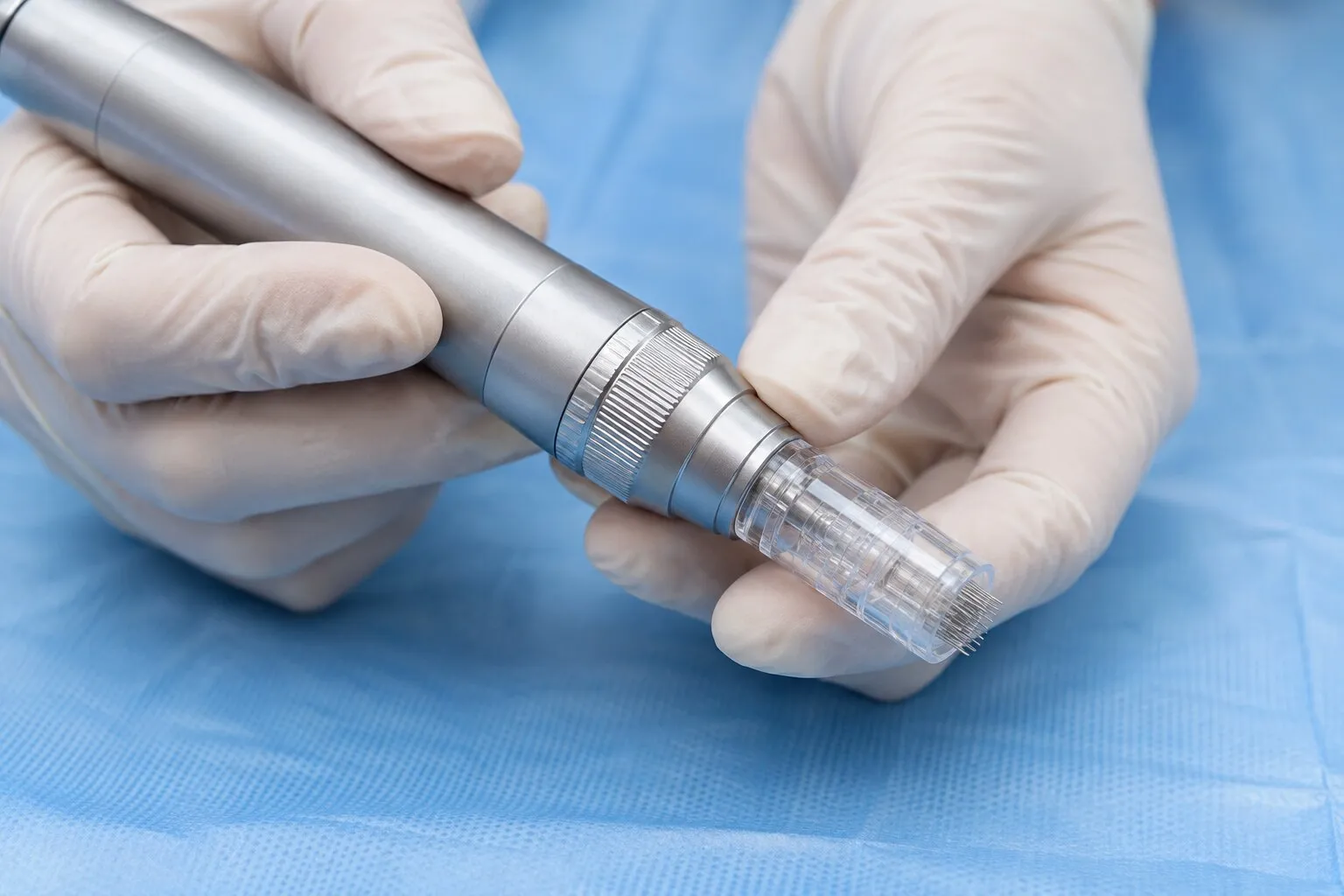 Gloved hands holding a microneedling pen with a sterile tip